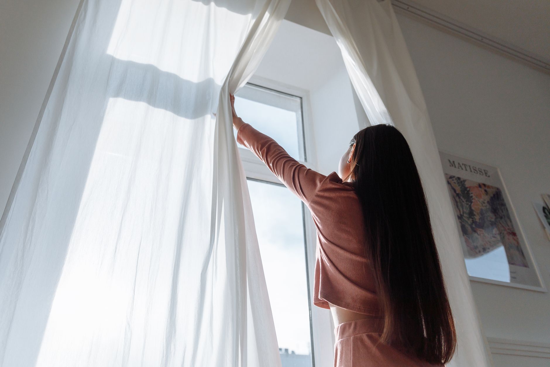 朝にカーテンを開けて光を入れる女性のイメージ