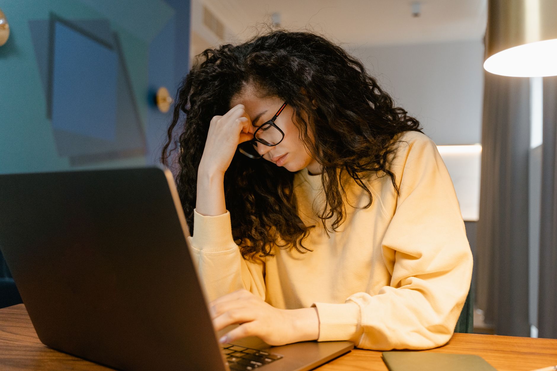 デスクで頭を押さえてだるそうにしている女性のイメージ