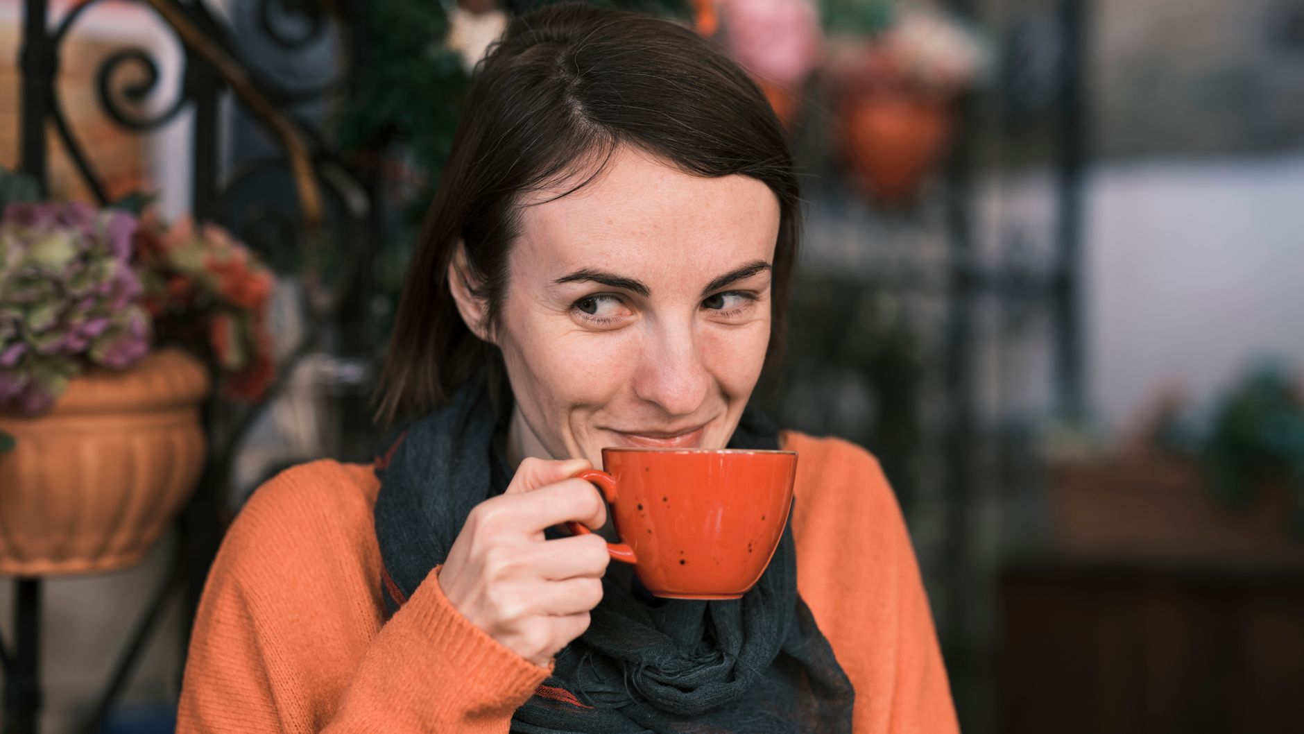 ストールを首に巻いて温かい飲み物でくつろぐ女性のイメージ